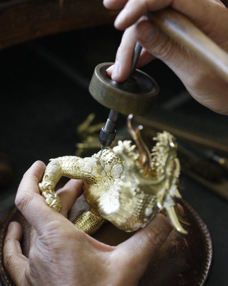A gem setter’s hands setting diamonds on a gold dragon sculpture