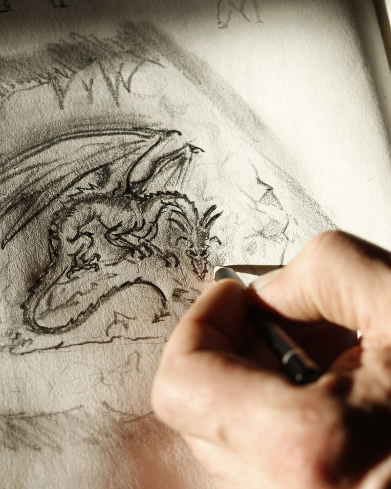 A hand sketching a dragon in pencil