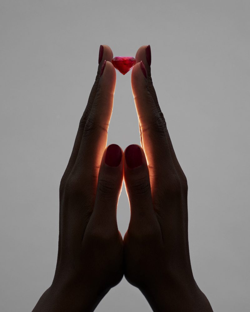 Two hands holding a ruby against a grey background